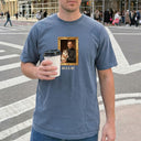 Person wearing a blue t-shirt with a graphic of a man and a dog, holding a coffee cup on a city street.